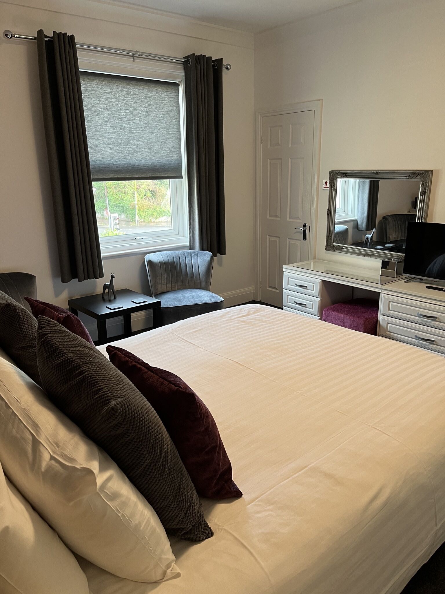 Una habitación de hotel con una cama grande, un escritorio, una silla, un aparador y un espejo.