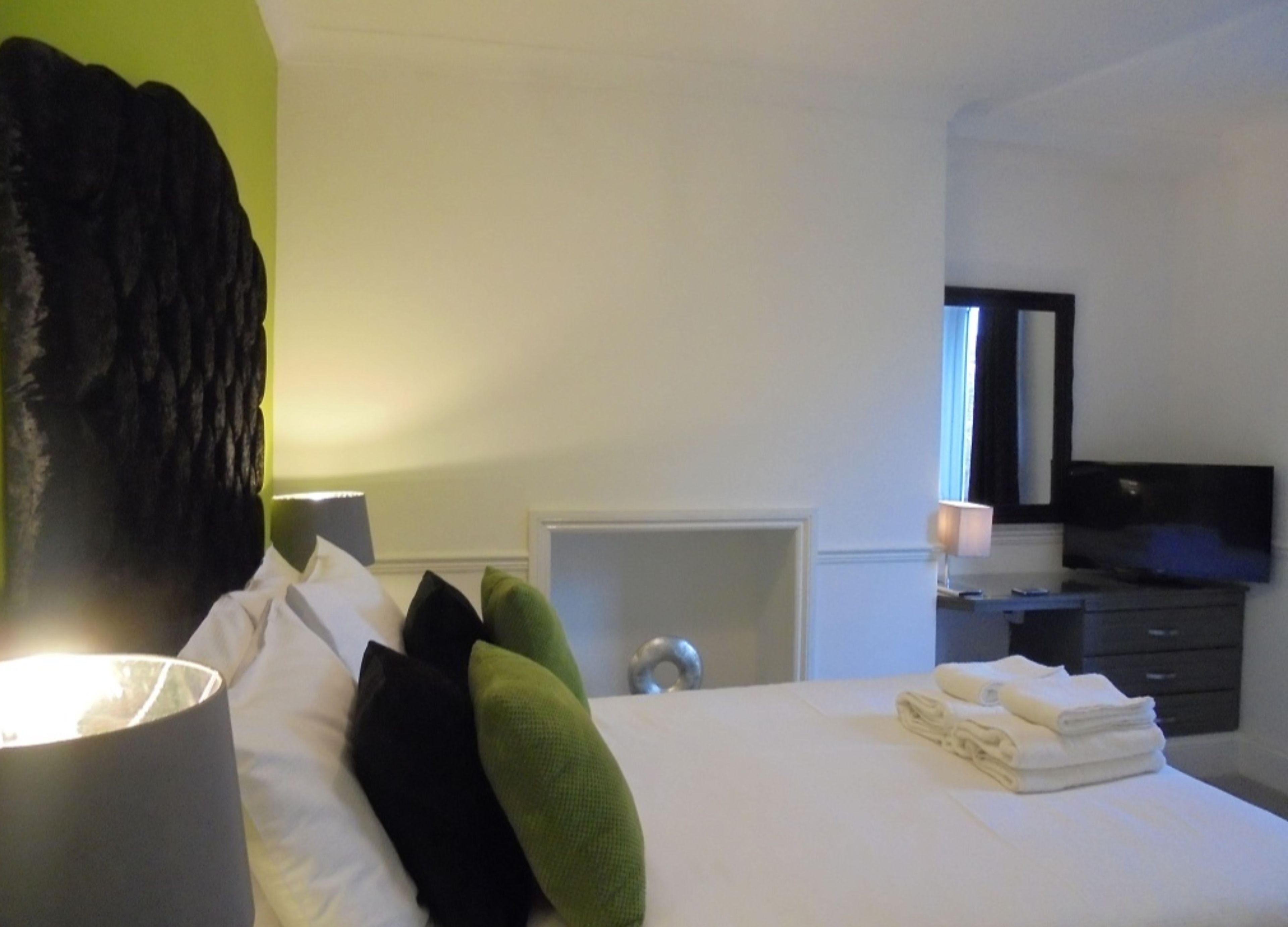 Une chambre d’hôtel équipée d’un lit, d’un bureau, d’une chaise, d’une lampe, d’un miroir et d’un téléviseur.