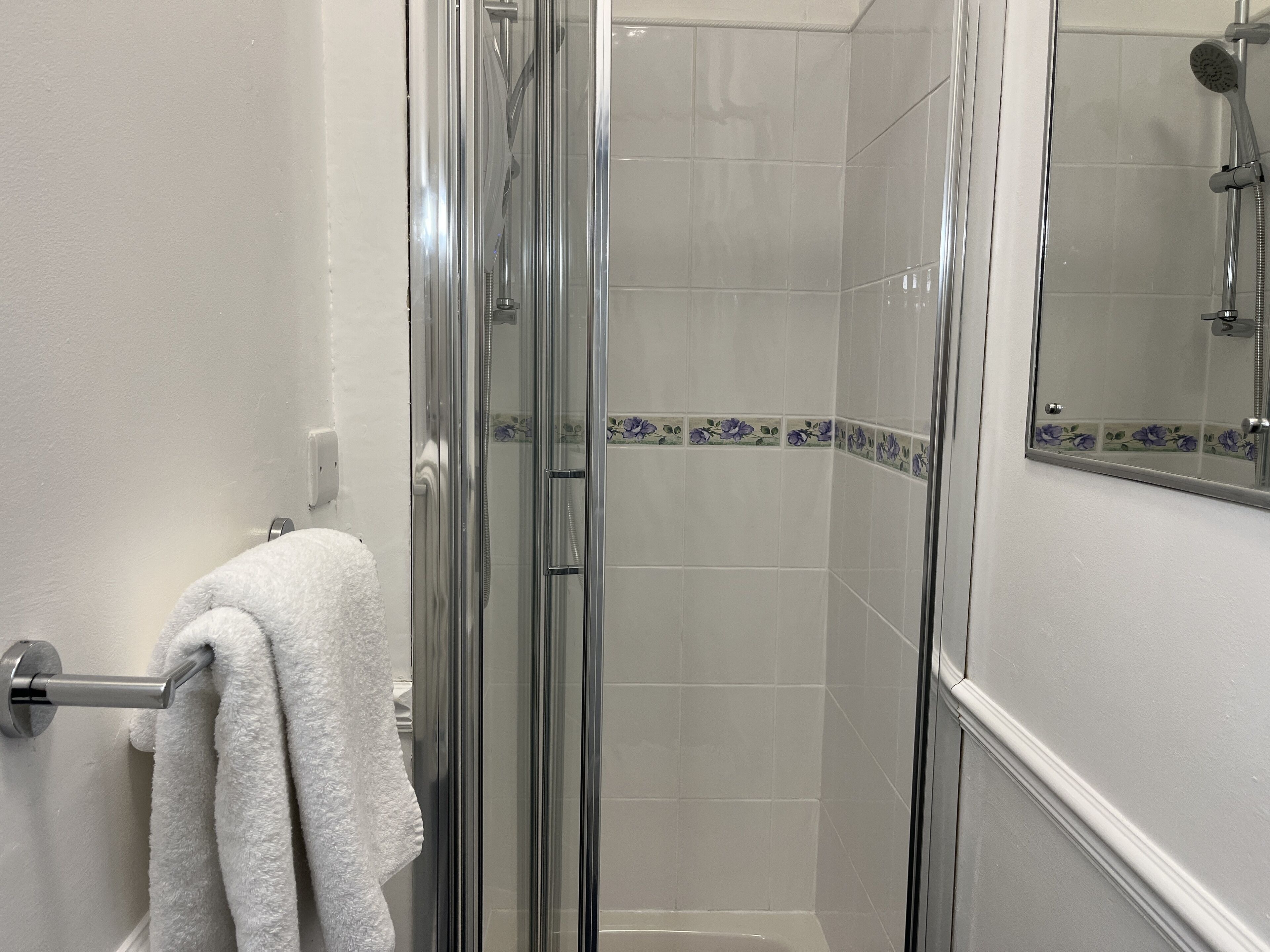 A glass-enclosed shower with a white tiled wall and a floral border.