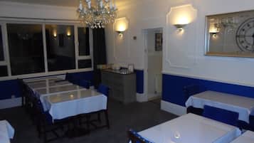 A dining area with tables and chairs, a chandelier, and wall-mounted lighting.