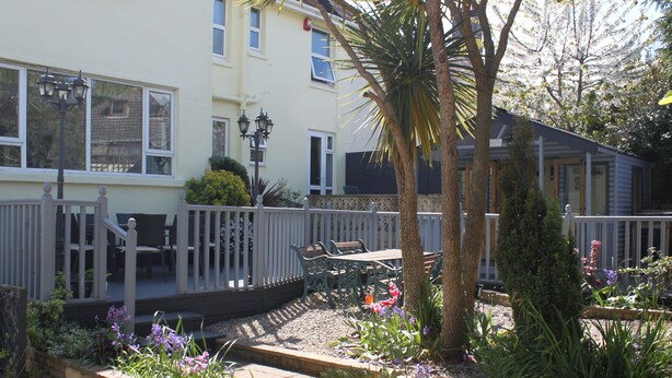 A garden with a wooden deck, outdoor seating, and various plants. - The Millbrook B & B (Torquay)