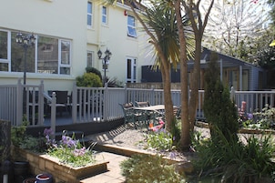 A garden with a wooden deck, outdoor seating, and various plants.