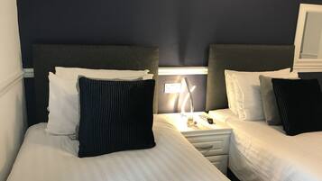 A hotel room with two beds, each with white linens and dark headboards. There is a nightstand with a lamp and a remote control between the beds.