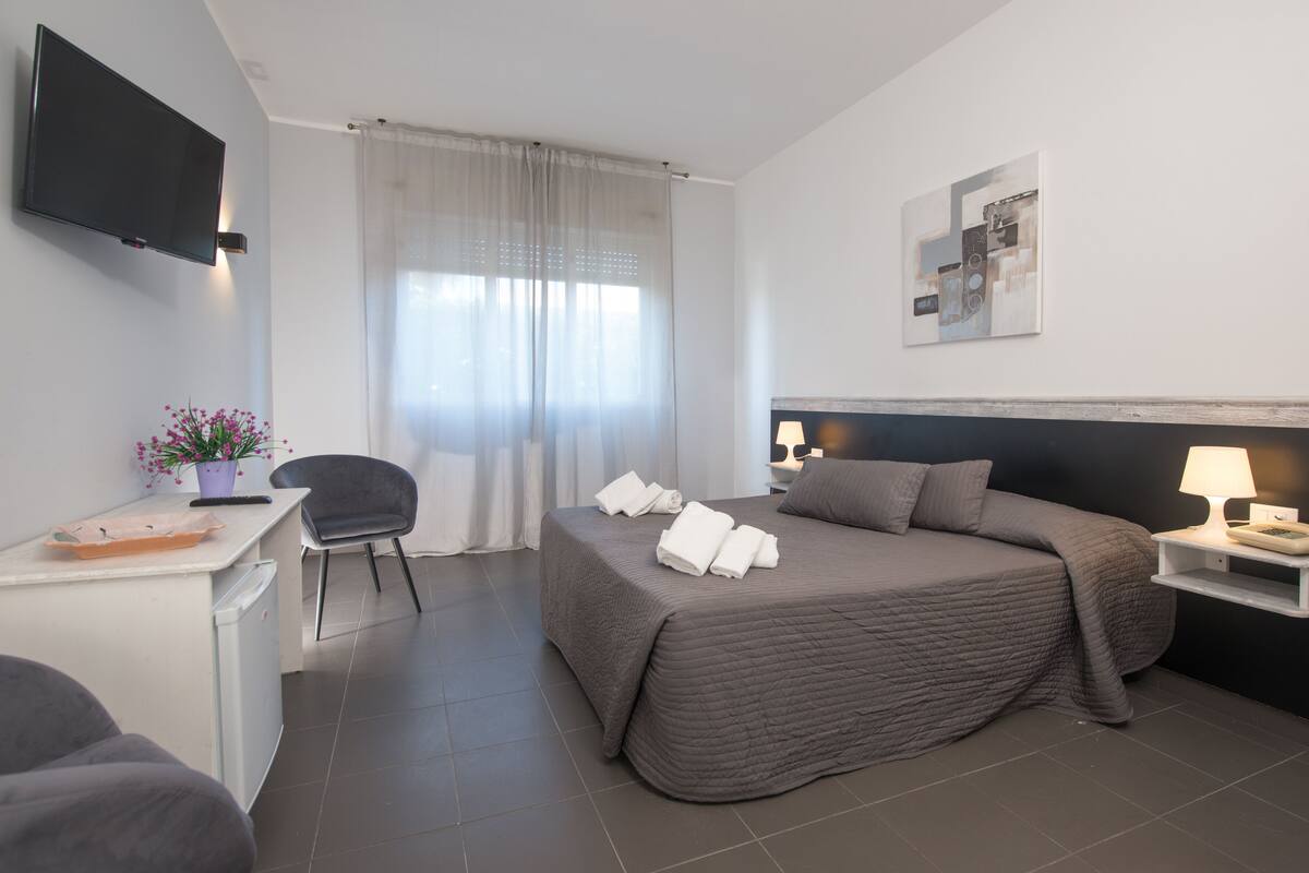 A hotel room with a bed, a desk, a chair, a TV, and a painting on the wall.