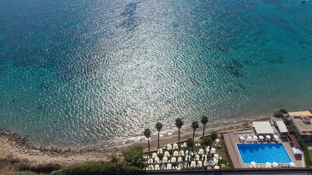 An aerial view of a beach resort with a swimming pool, sun loungers, and palm trees. - Hotel President Sea Palace (Noto)