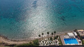 An aerial view of a beach resort with a swimming pool, sun loungers, and palm trees. - Hotel President Sea Palace (Noto)
