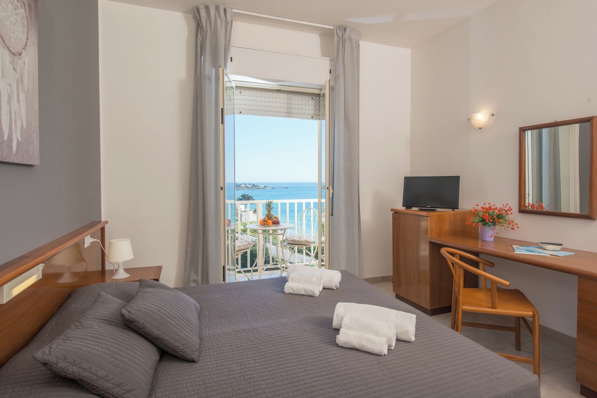 Habitació d'hotel amb llit, escriptori, cadira, televisió i un balcó amb vista al mar.