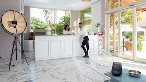 A modern reception area with a marble floor, a white reception desk, and a large window offering a view of greenery outside. - Hotel President Sea Palace (Noto)