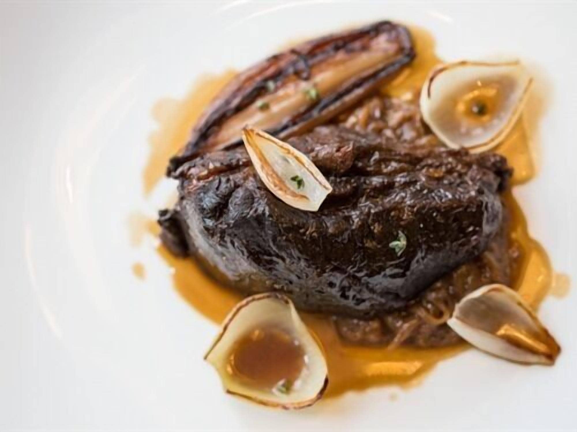Een bord met vlees, mogelijk steak, vergezeld van kokkels en saus.