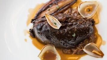 Een bord met vlees, mogelijk steak, vergezeld van kokkels en saus.