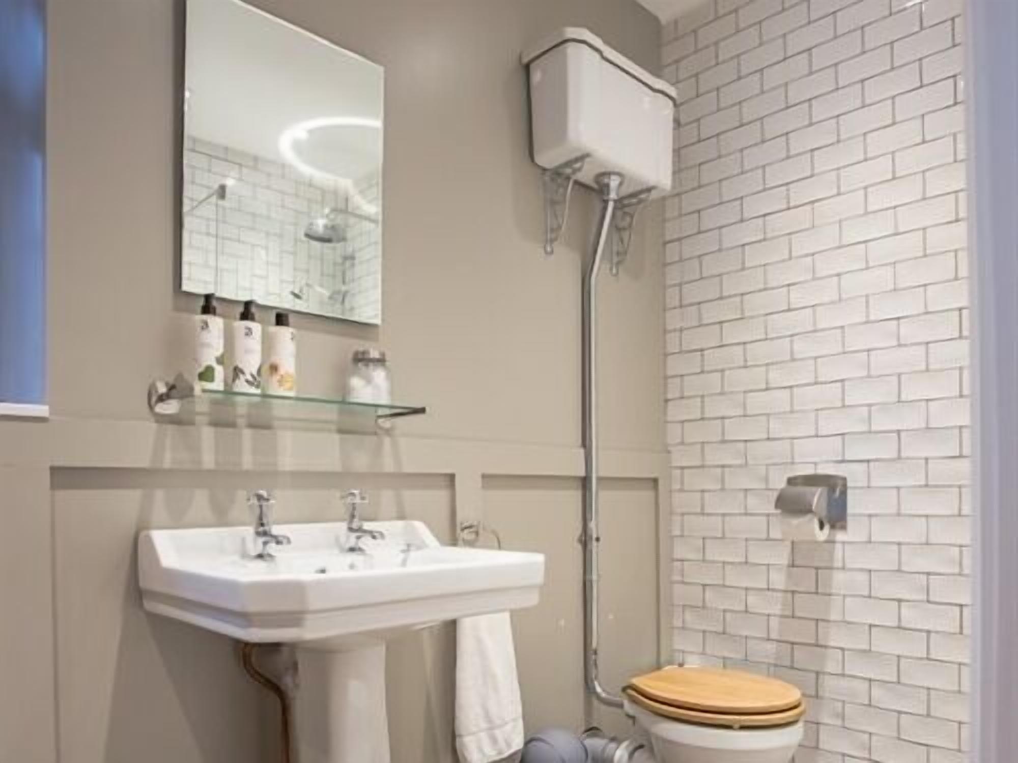 A bathroom with a white sink, mirror, and toilet. There is a shower area with a glass door and a white tiled wall.