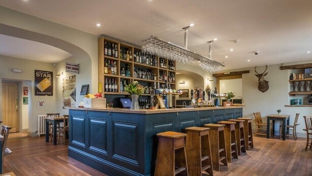 A bar area with a long counter, stools, and shelves stocked with bottles. - The Redan (Radstock)