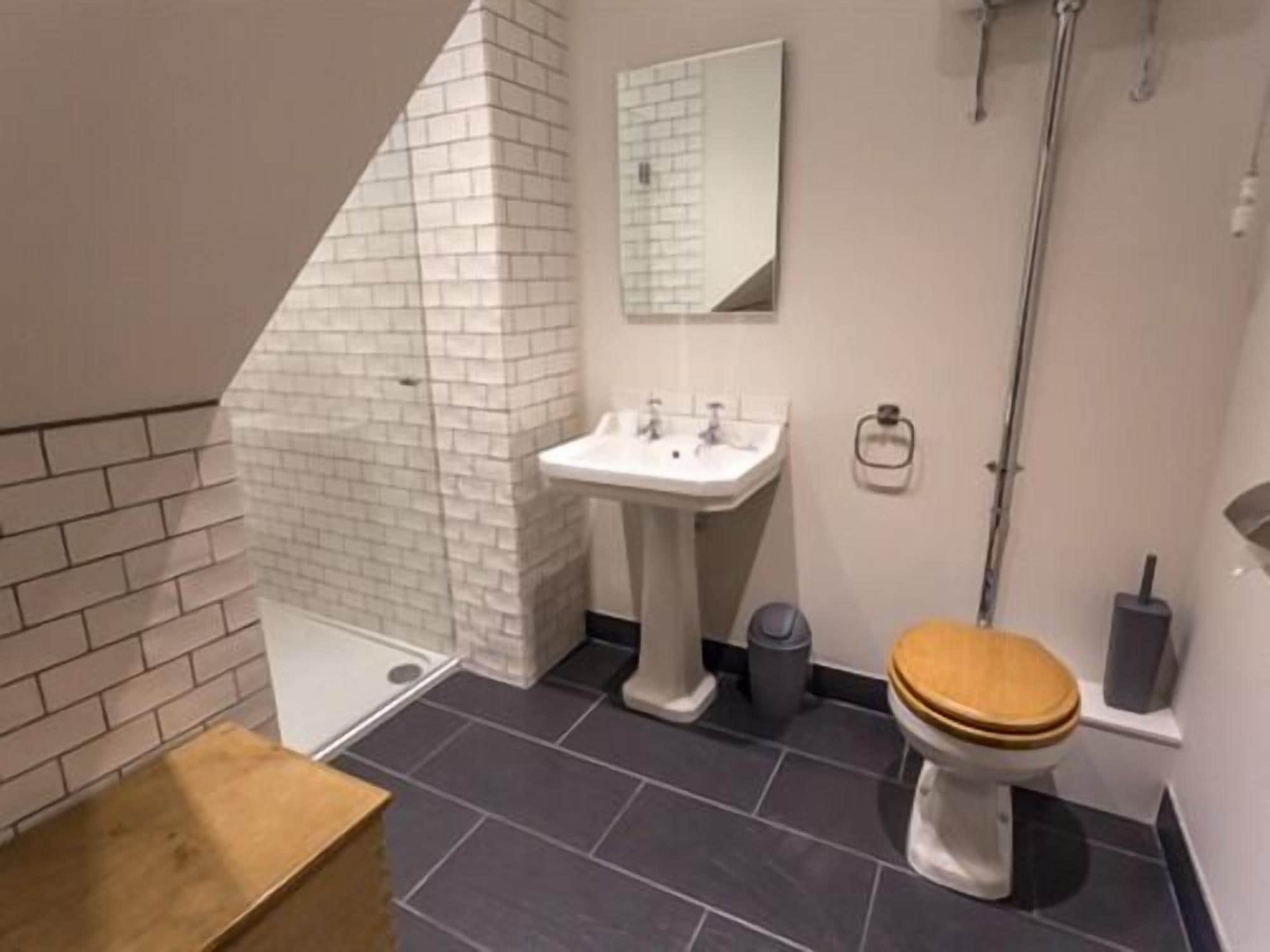 A bathroom with a white sink, a wooden toilet, a mirror, and a shower area.