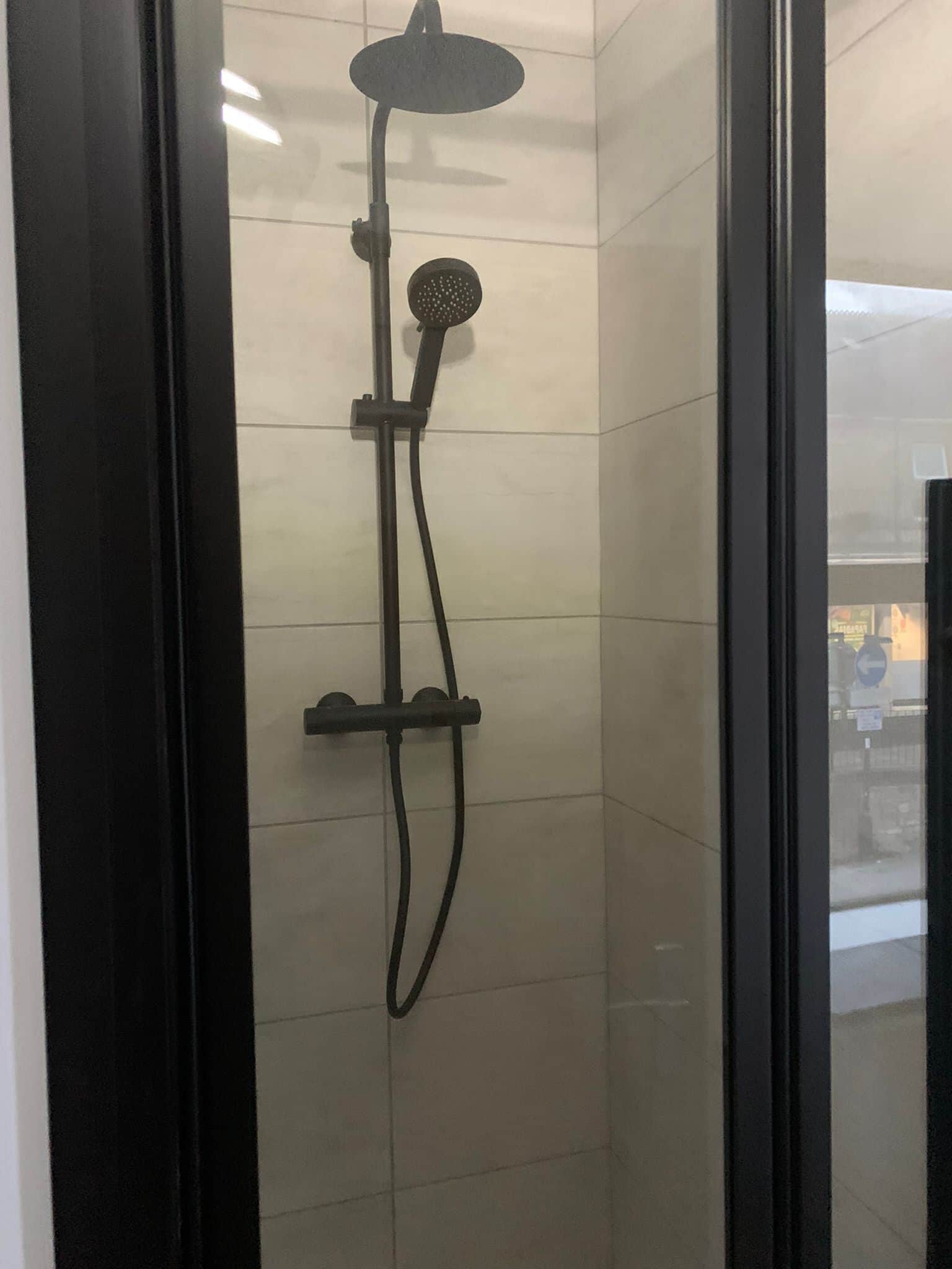 A glass-enclosed shower with a handheld showerhead and a fixed wall-mounted head.