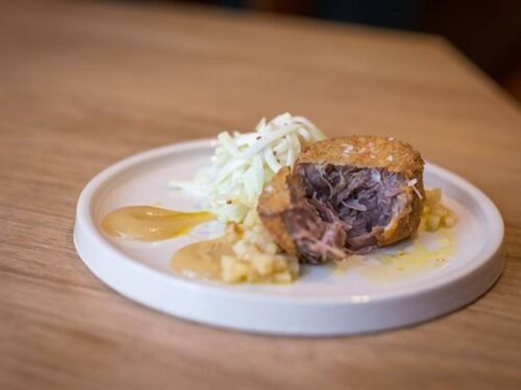 A plate with a meat dish, possibly a steak, accompanied by a side of shredded vegetables and a dollop of sauce.
