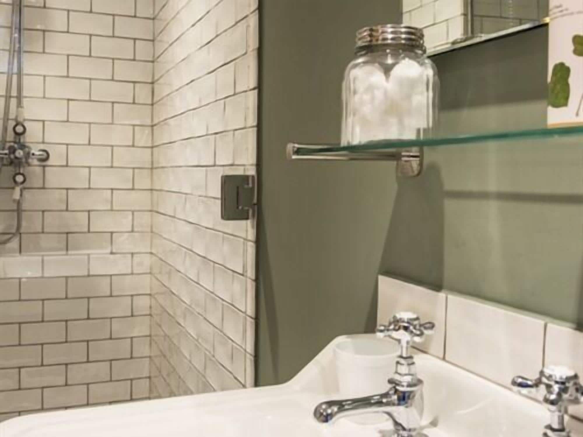 Un bagno con pareti piastrellate di bianco, uno scaffale in vetro con un vasetto e un lavandino bianco.