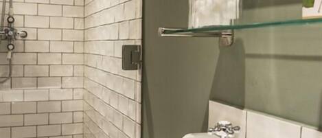 Un bagno con pareti piastrellate di bianco, uno scaffale in vetro con un vasetto e un lavandino bianco.