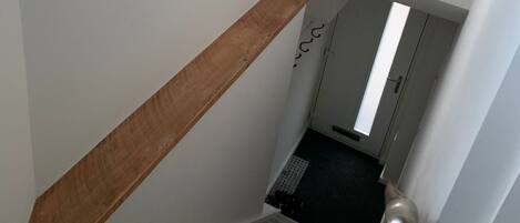A staircase with a wooden handrail, a small shelf with a white container, and a door with a light fixture.