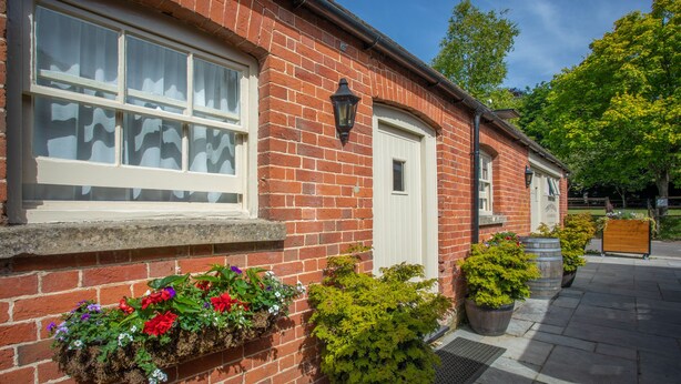 A brick building with white-framed windows, a door, and a small porch area with flower boxes and potted plants. - The White Lion (Southampton)