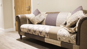 A brown leather sofa with patterned cushions against a plain wall and wooden floor. - The White Lion (Southampton)