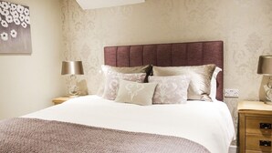 A neatly made bed with a headboard, two bedside tables with lamps, and a wooden nightstand with drawers. - The White Lion (Southampton)