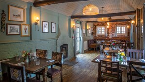 A rustic dining area with wooden tables and chairs, a brick fireplace, and framed pictures on the walls. - The White Lion (Southampton)