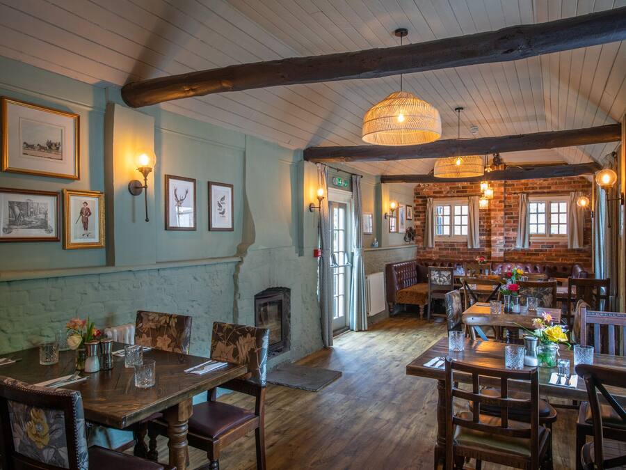 A rustic dining area with wooden tables and chairs, a brick fireplace, and framed pictures on the walls.