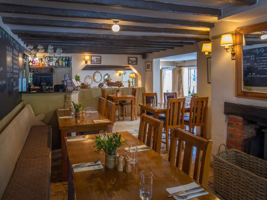 Een gezellig restaurant met houten tafels en banken, een bar met flessen en een menukaart op een schoolbord.