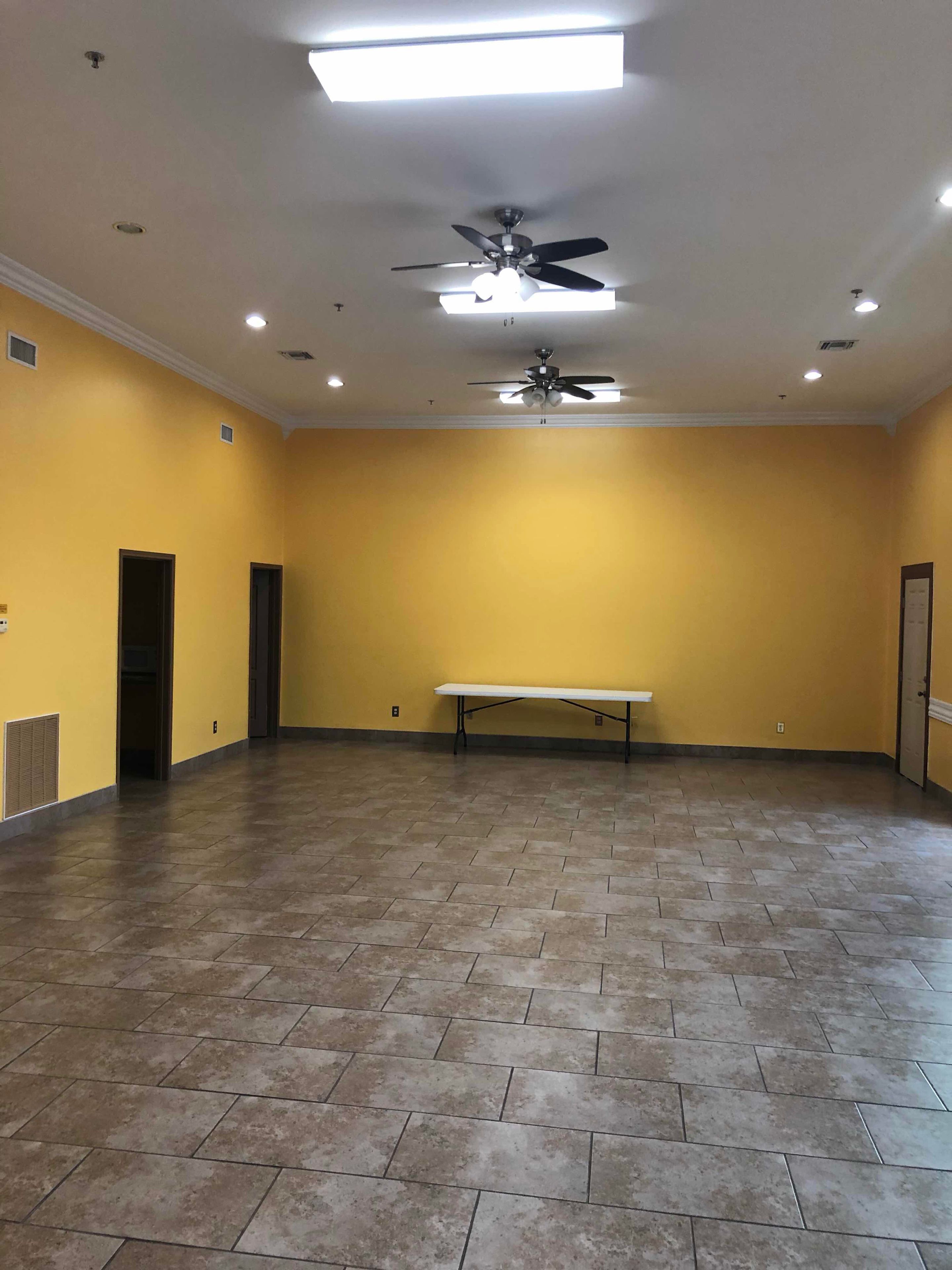 A spacious room with yellow walls, a ceiling fan, recessed lighting, and a bench.