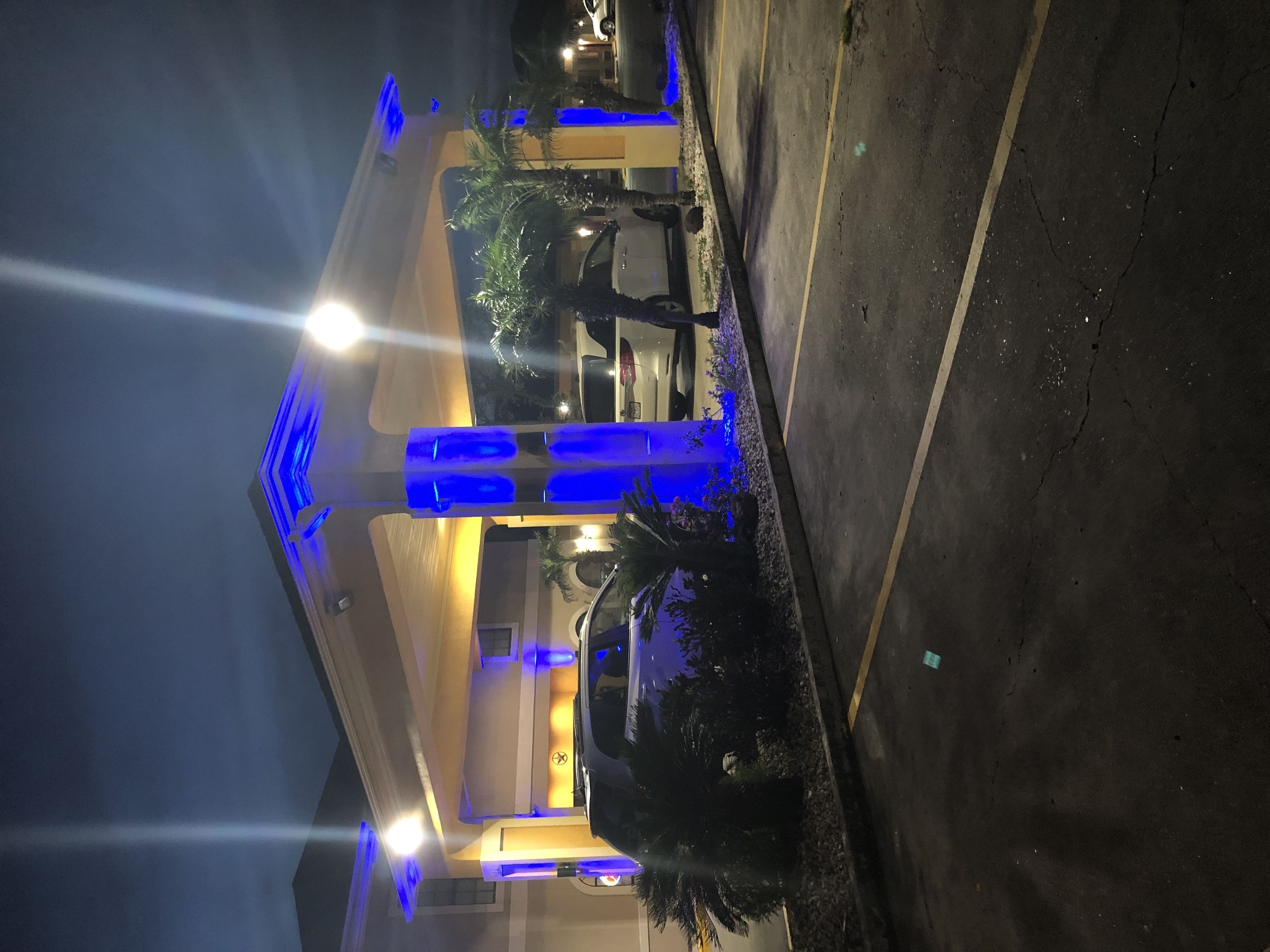 Een nachtzicht van een gebouw met blauwe verlichtingsaccenten, een parkeerplaats en een geparkeerd voertuig.