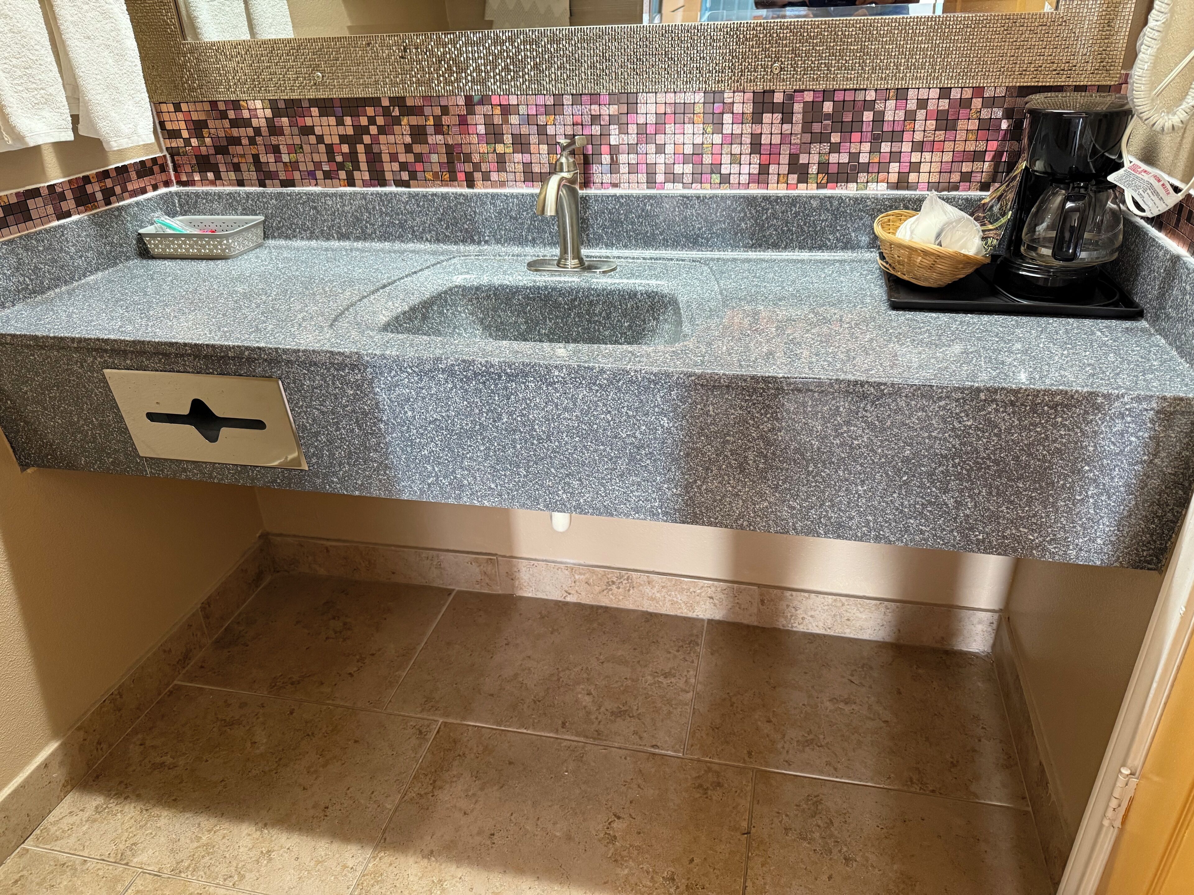 A bathroom with a granite countertop, a sink, a faucet, a coffee maker, and a tiled backsplash.