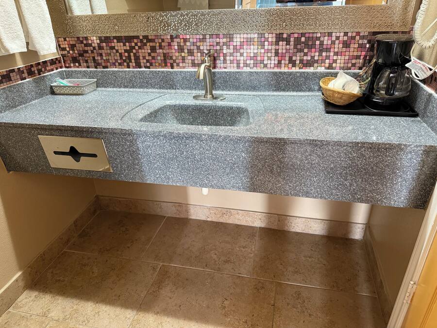 A bathroom with a granite countertop, a sink, a faucet, a coffee maker, and a tiled backsplash.