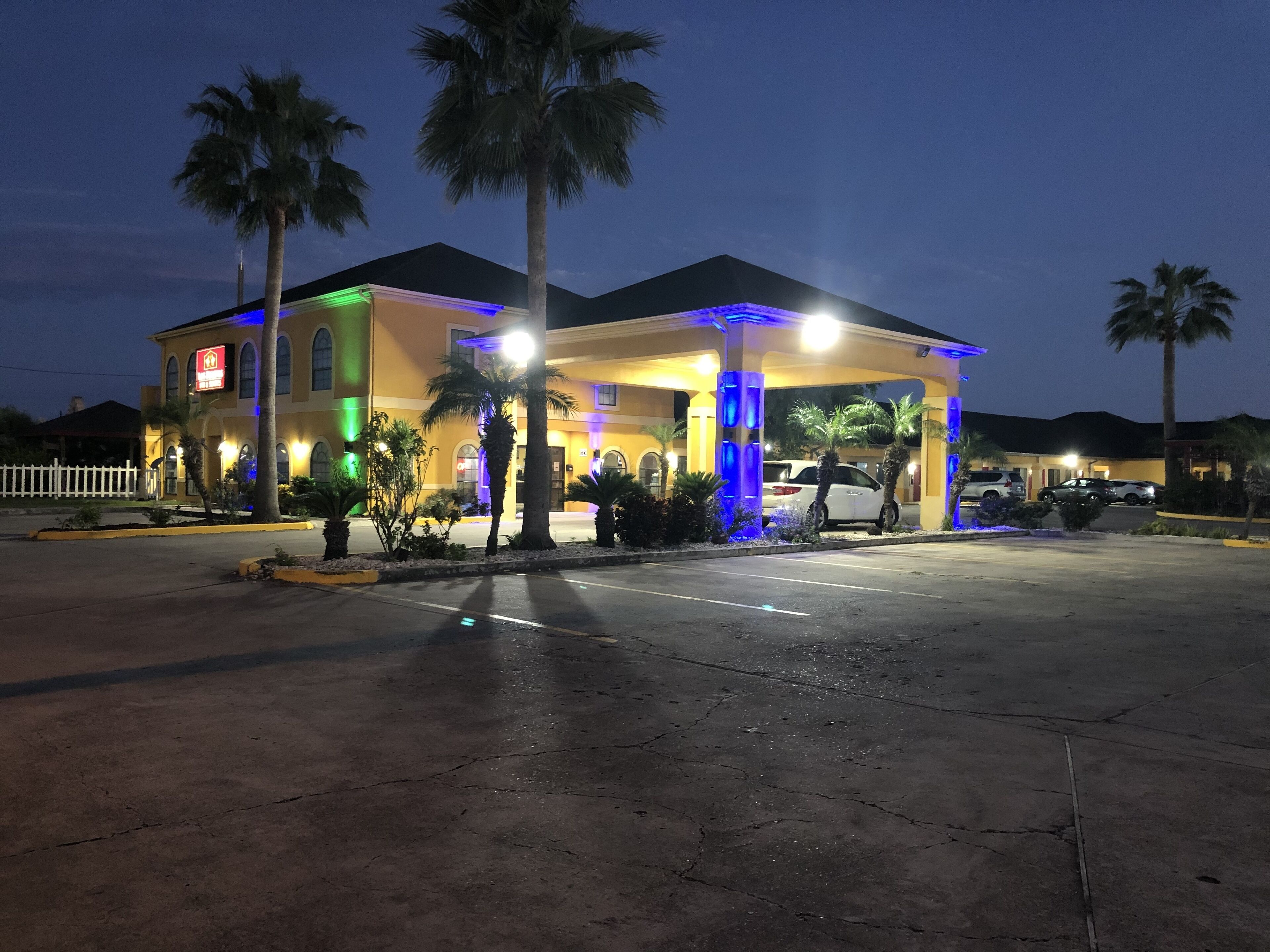 A hotel with a covered parking area, palm trees, and a well-lit facade.