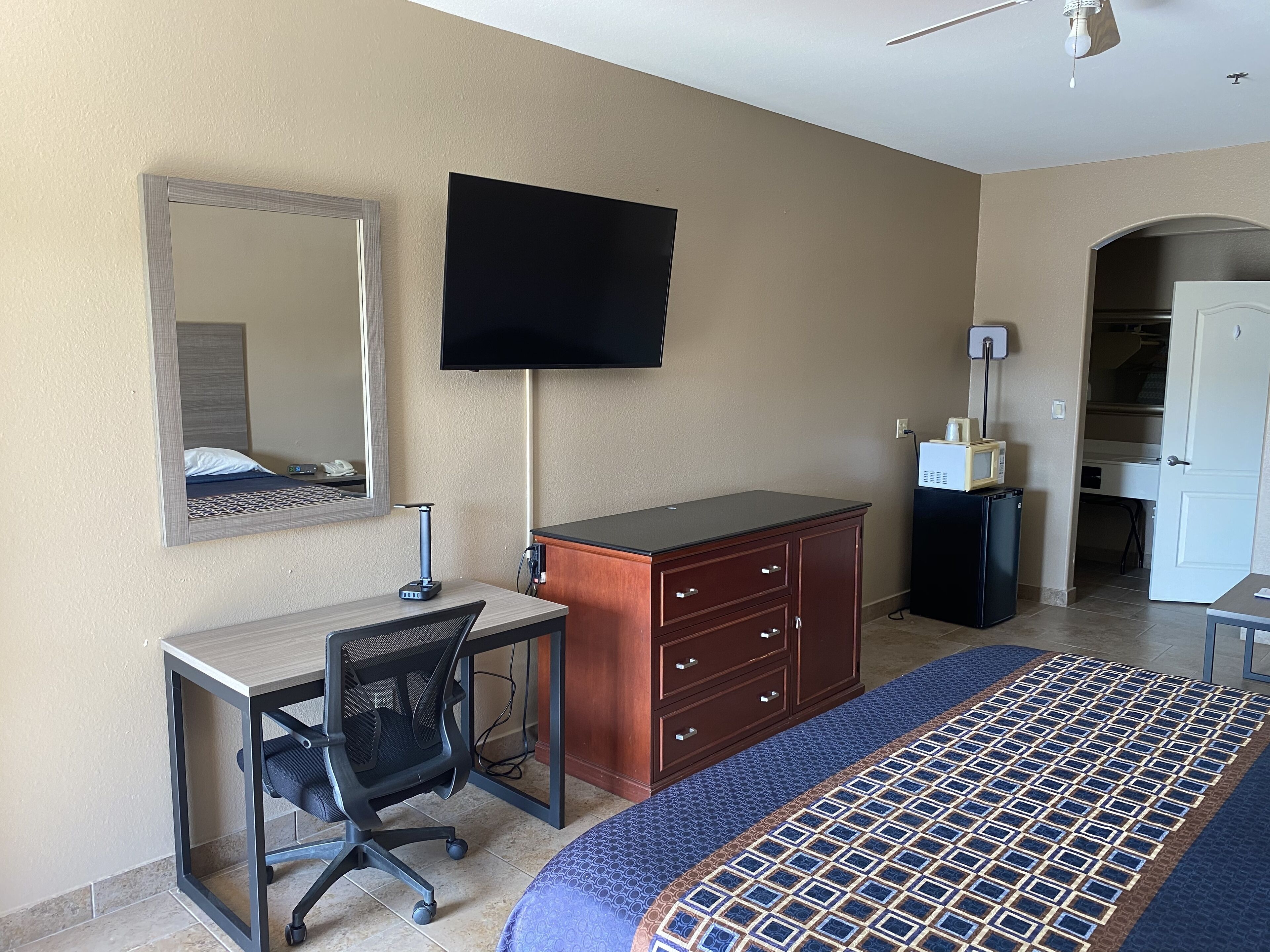 Habitación de hotel con cama, escritorio, silla, televisor, armario y microondas.