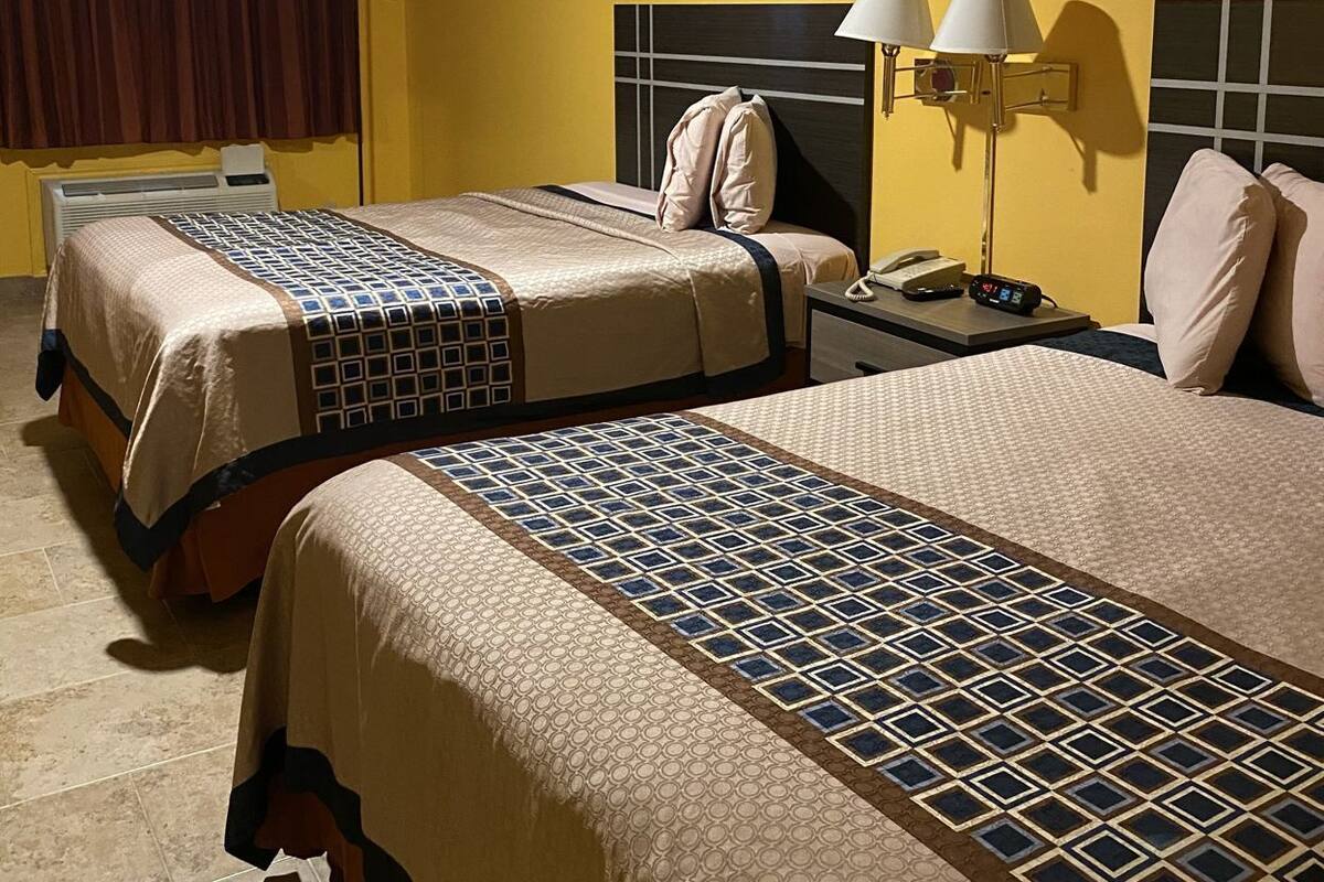 Ein Hotelzimmer mit zwei Betten, einem Deckenventilator, einem Bild an der Wand und einem Nachttisch mit Lampen.