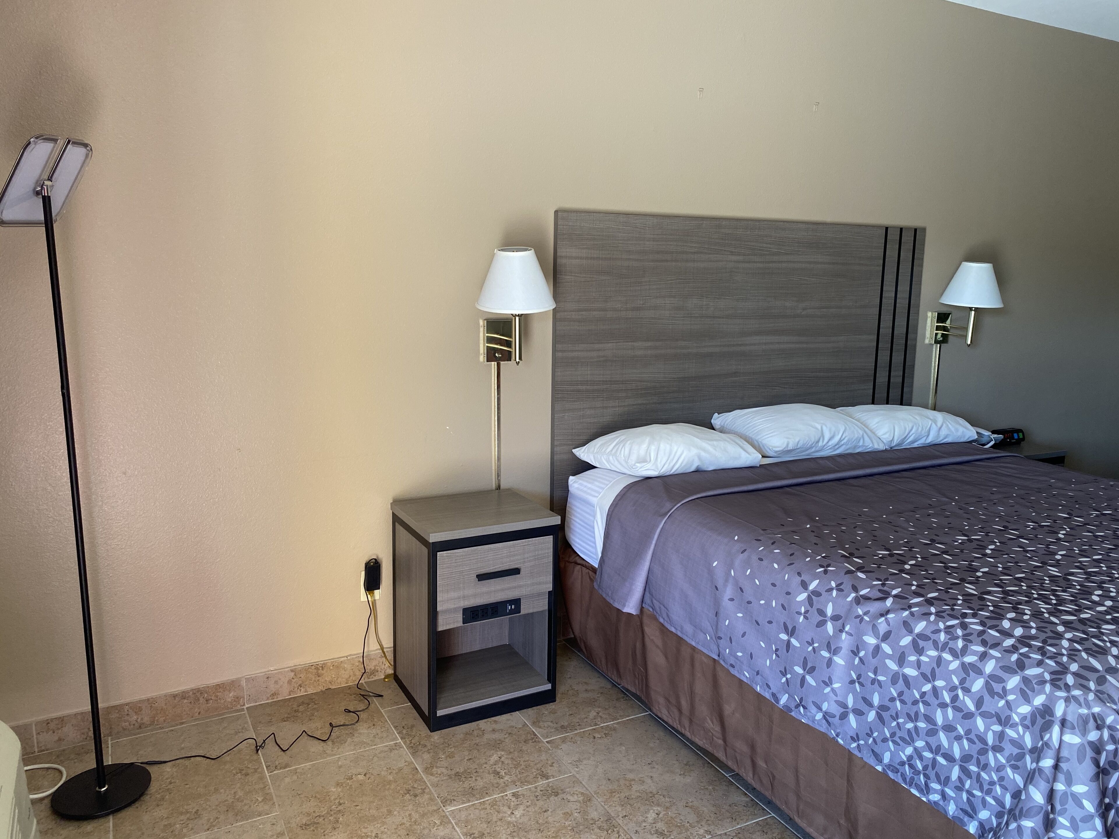 Habitación de hotel con cama, dos lámparas de noche, mesita de noche y toma de corriente.
