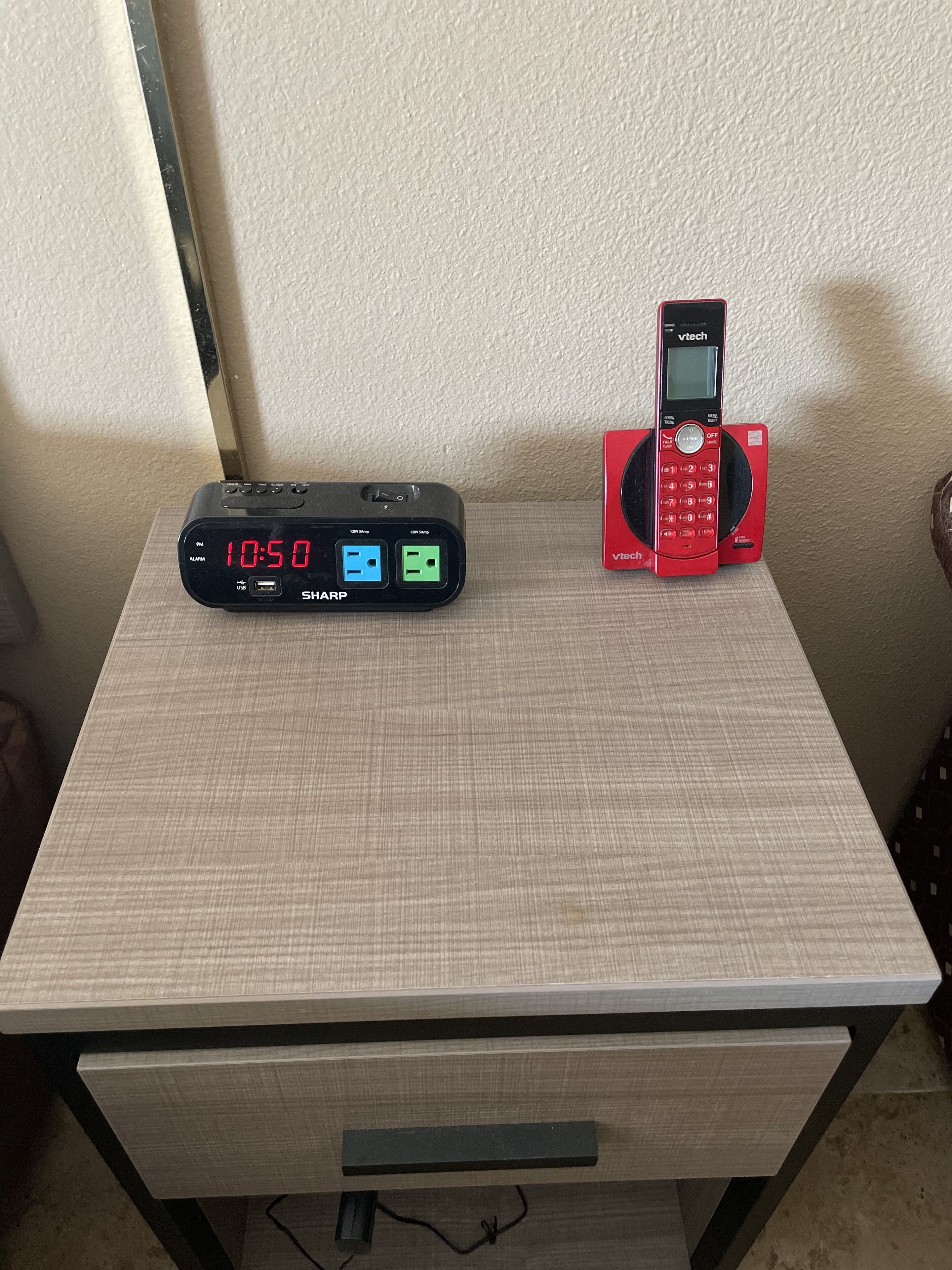 A desk with a digital clock displaying 10:50, a red phone, and a USB charging station.