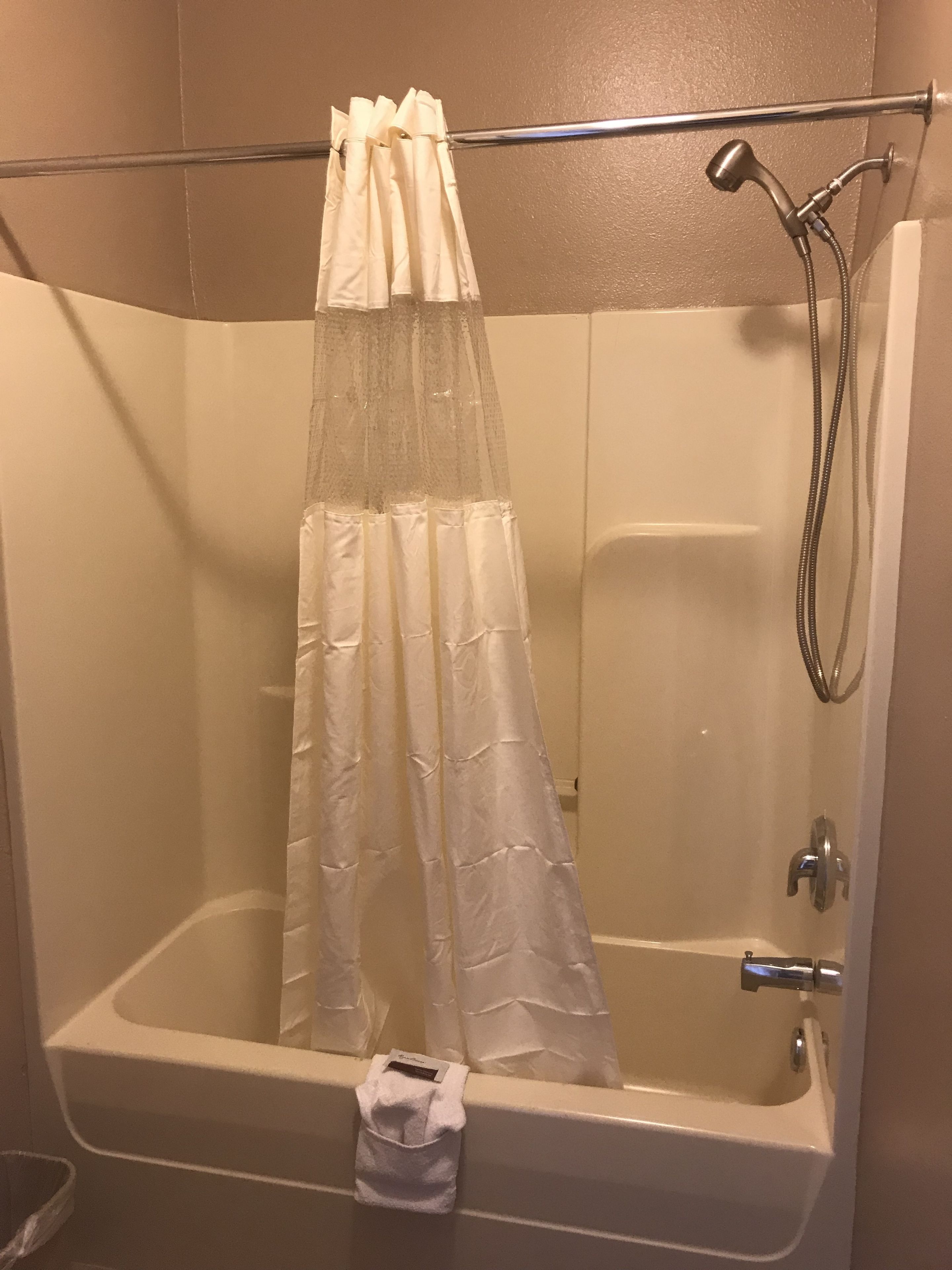 A shower with a white curtain, a handheld showerhead, and a handheld shower attachment.