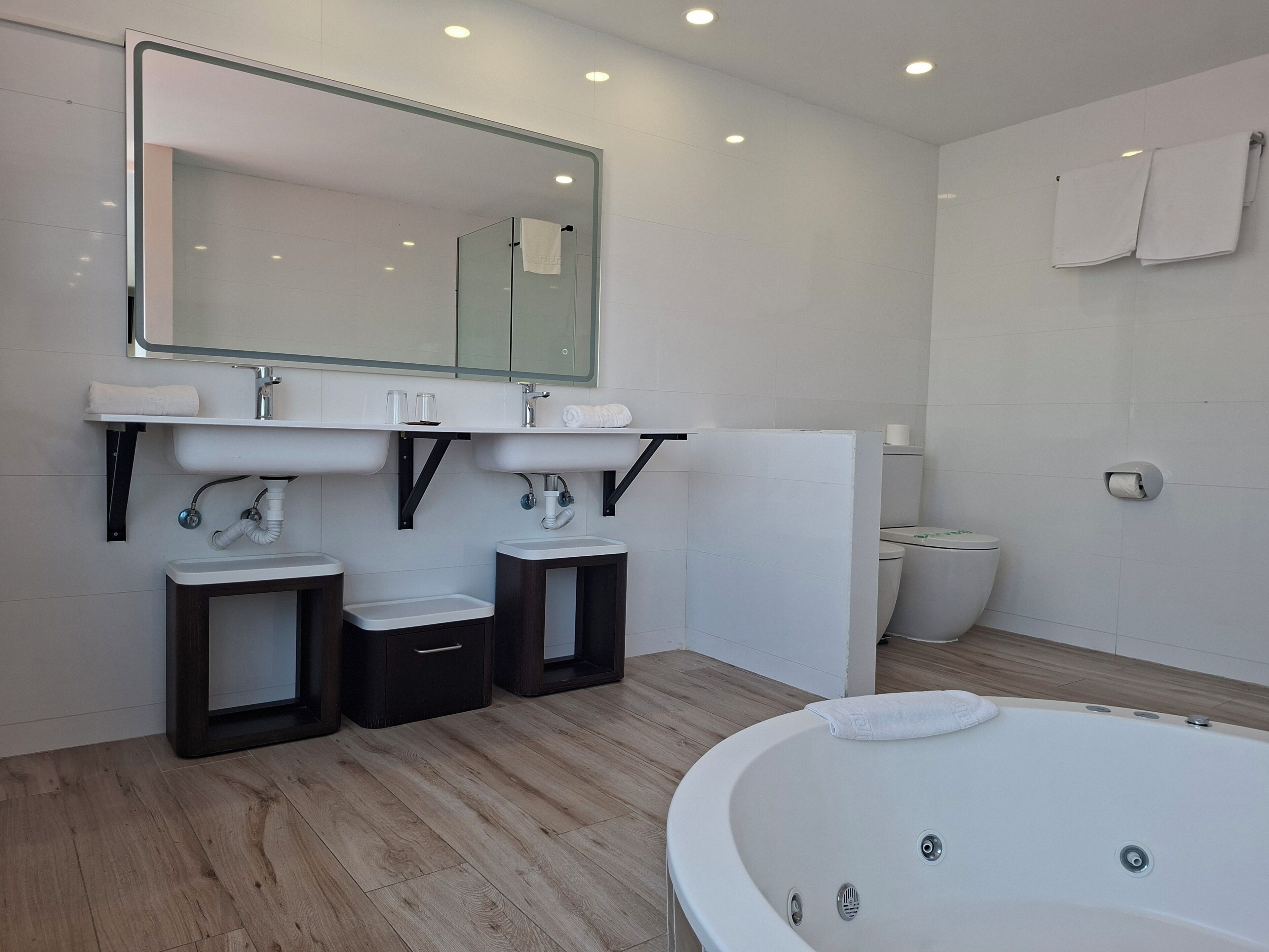 Ein modernes Badezimmer mit einer großen Badewanne, zwei Waschbecken, einer Toilette und einem Spiegel.