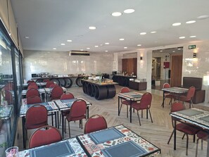 A modern restaurant with multiple dining tables and chairs, a counter with food items, and a glass wall offering a view. - Hotel 153 (Castelldefels)