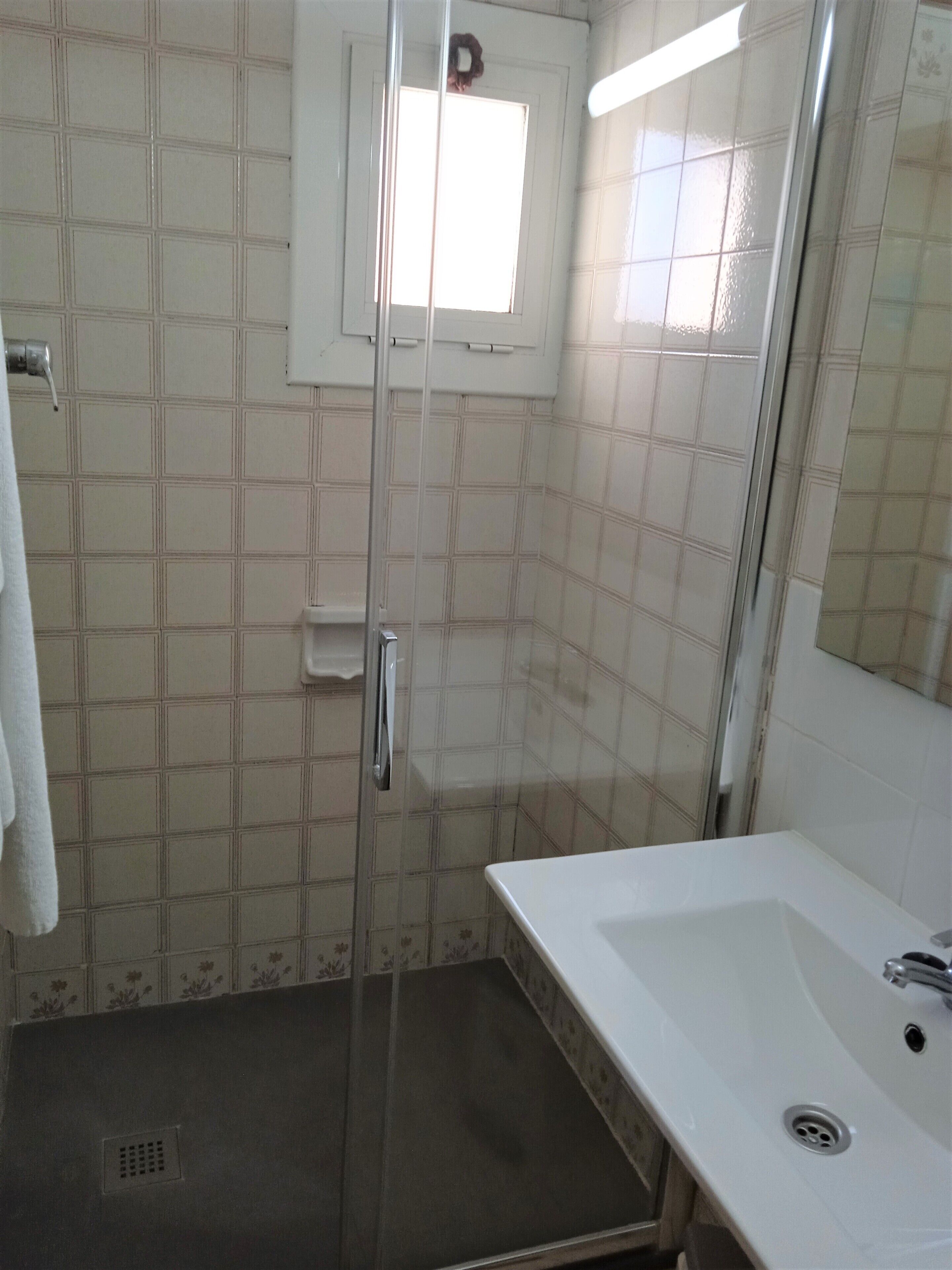 Een badkamer met een wit wastafelmeubel, een douchecabine met glazen wanden en een klein raam boven de deur.