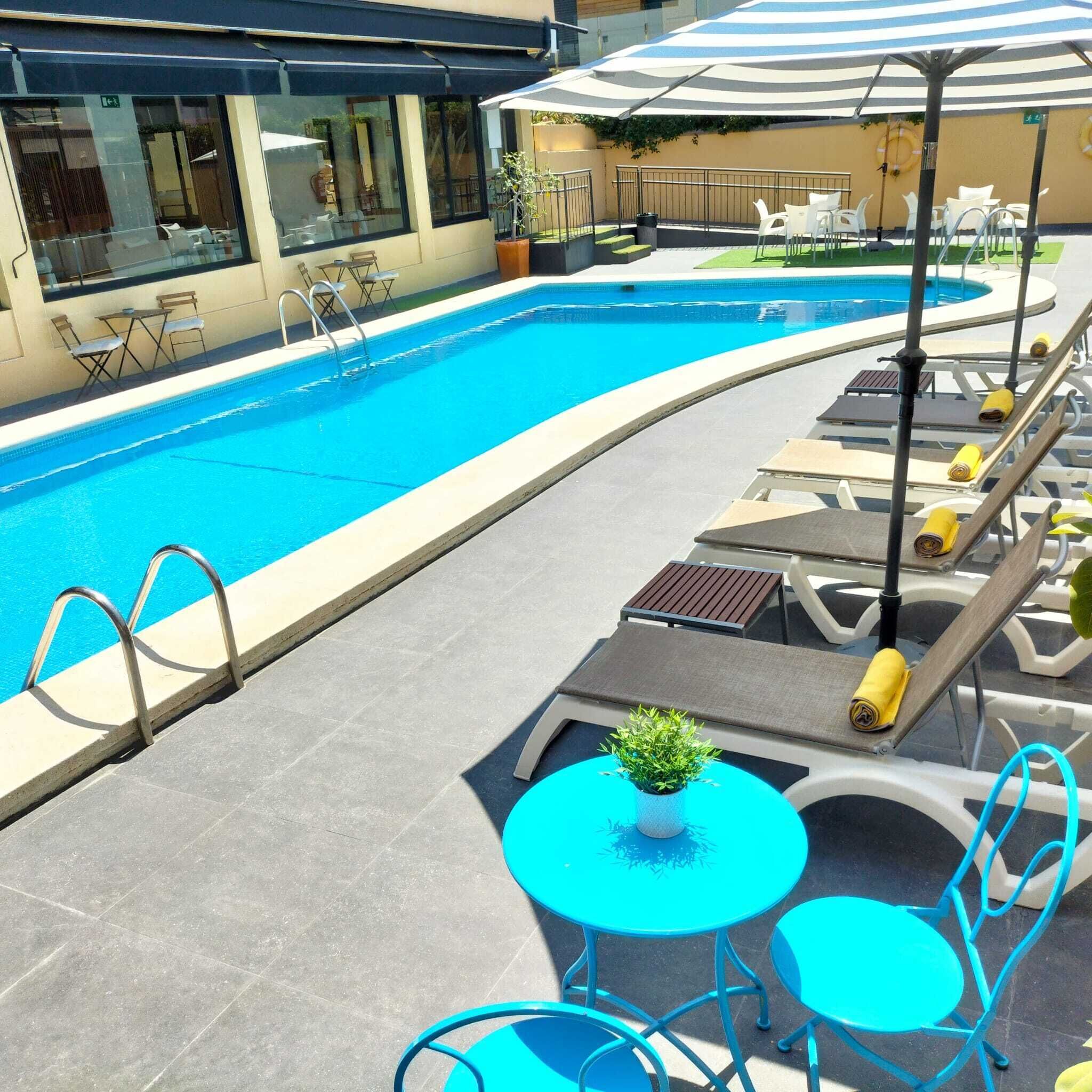 A swimming pool with lounge chairs and a table, surrounded by a building with large windows.