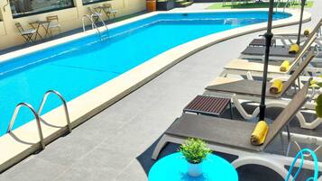 A swimming pool with lounge chairs and a table, surrounded by a building with large windows.