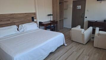 A hotel room with a large bed, a desk, a chair, a small table, and a TV.