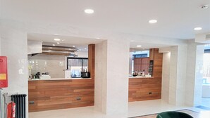 A modern hotel lobby with a reception desk, wooden paneling, and a green upholstered chair. - Hotel 153 (Castelldefels)