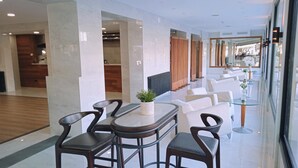 A modern hotel lobby with a seating area featuring a round table and four chairs, a small potted plant, and a glass partition. - Hotel 153 (Castelldefels)