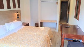 A hotel room with a large bed, a desk, a chair, a small table, a mirror, and a wardrobe.