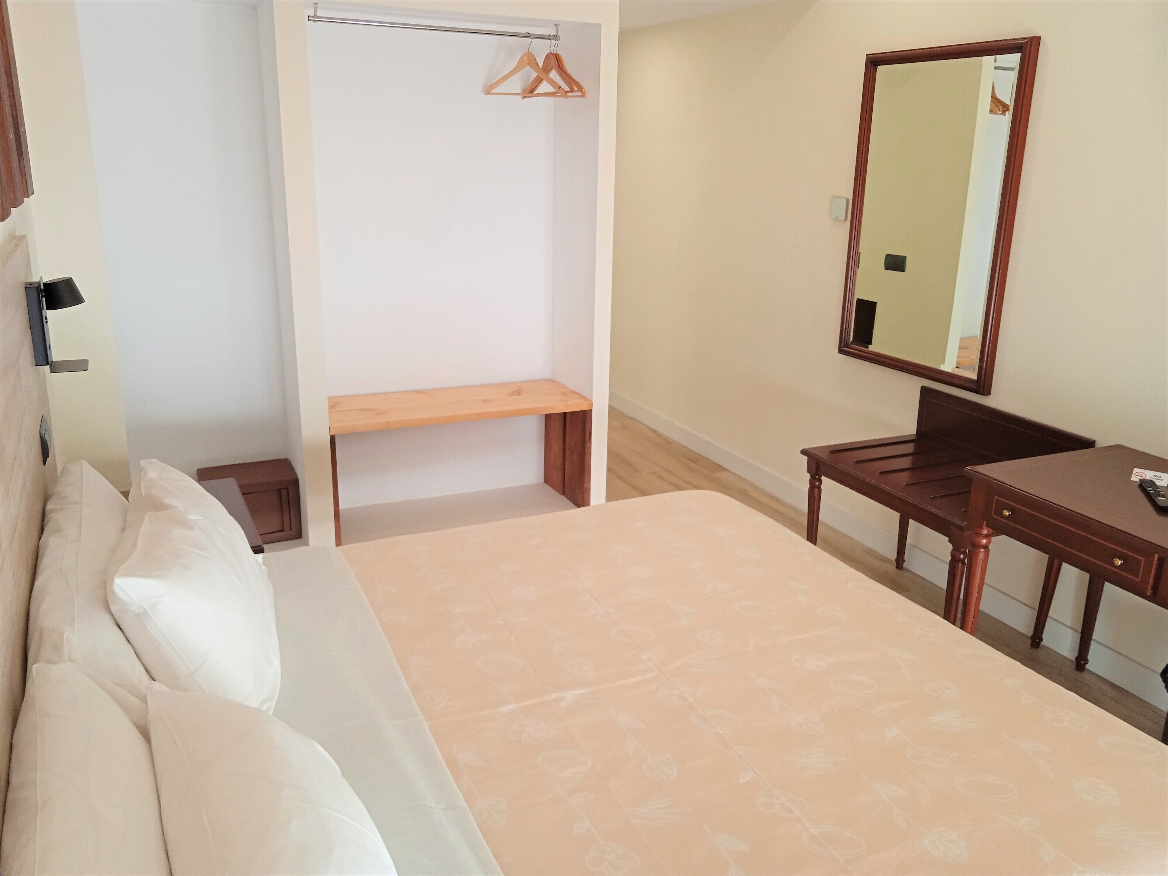 Un dormitorio con cama, banco de madera, escritorio y espejo.