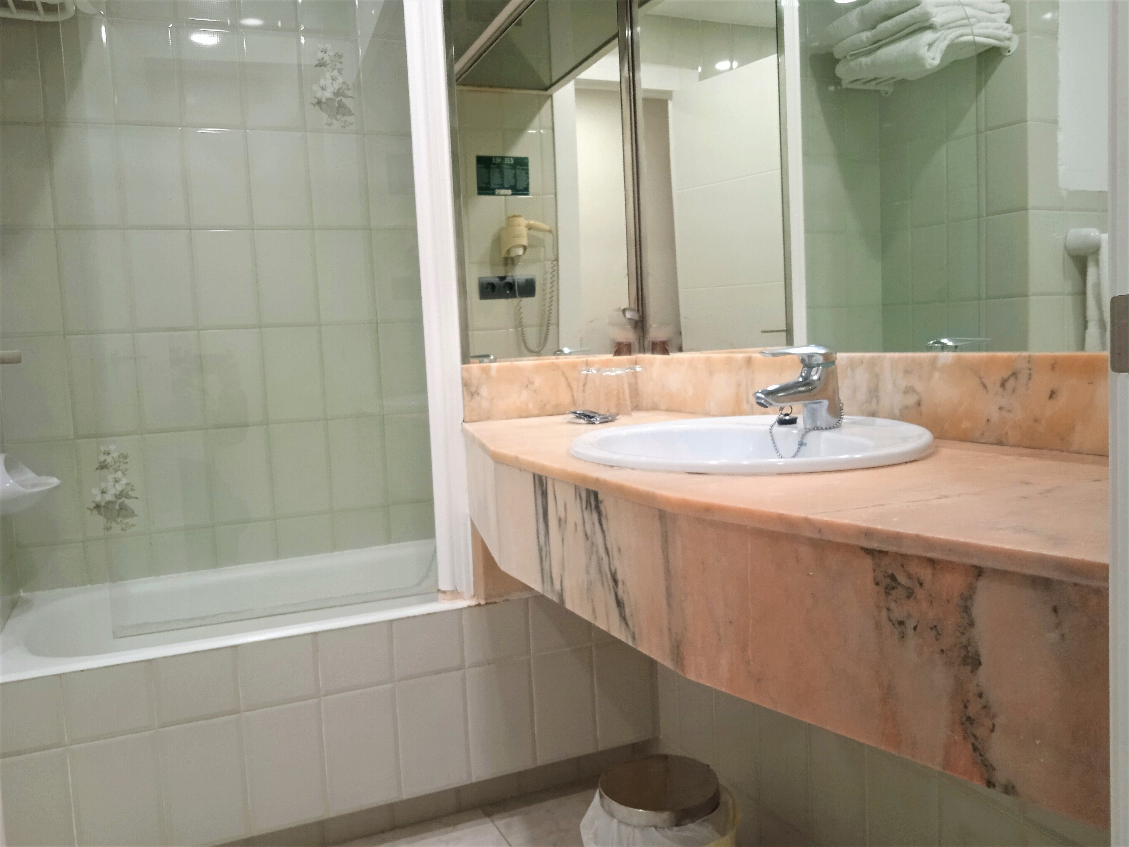 A bathroom with a glass shower enclosure, a sink with a marble countertop, and a mirror above the sink.