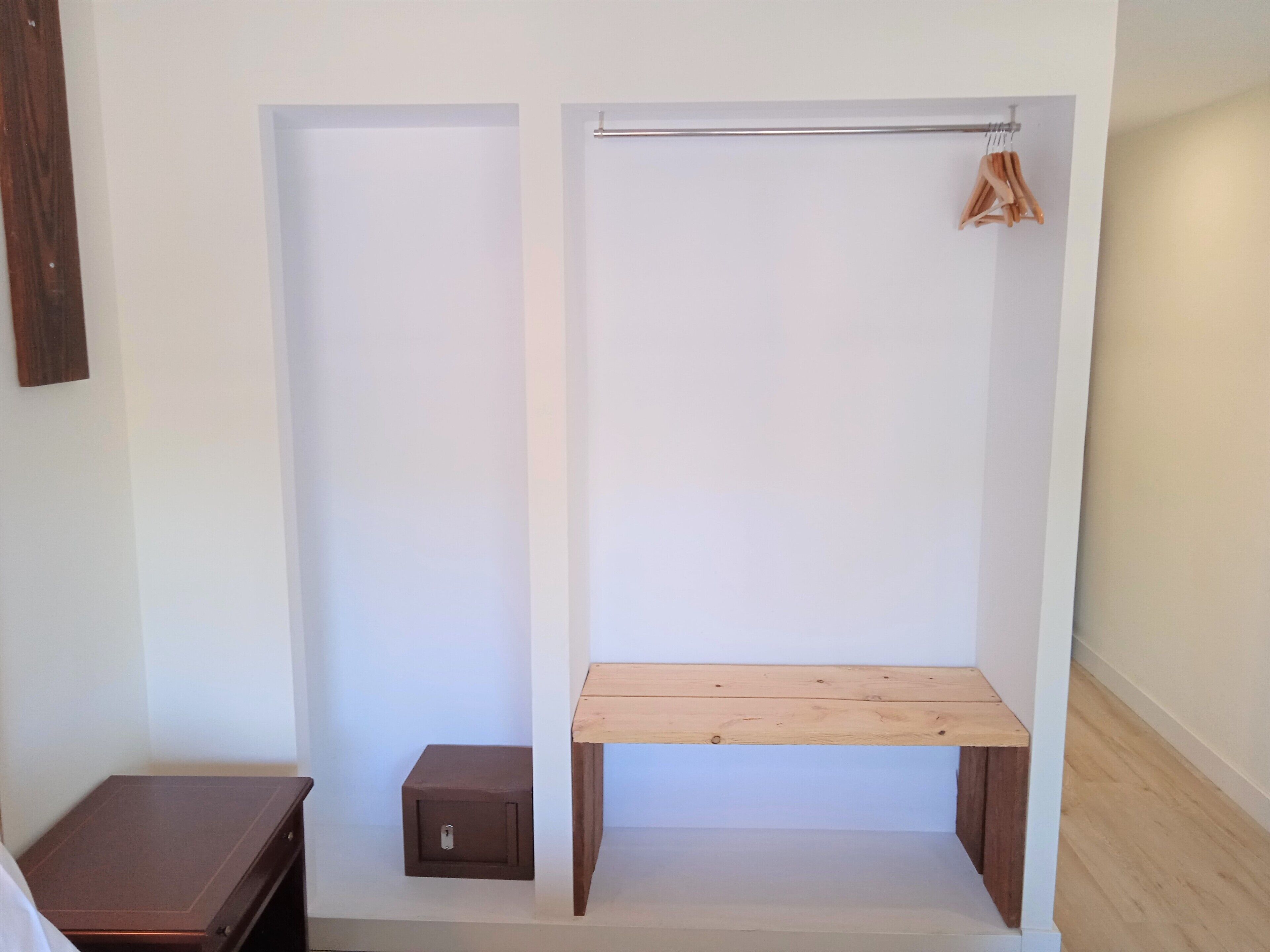A walk-in closet with a wooden bench, a hanging rod, and a small storage box.